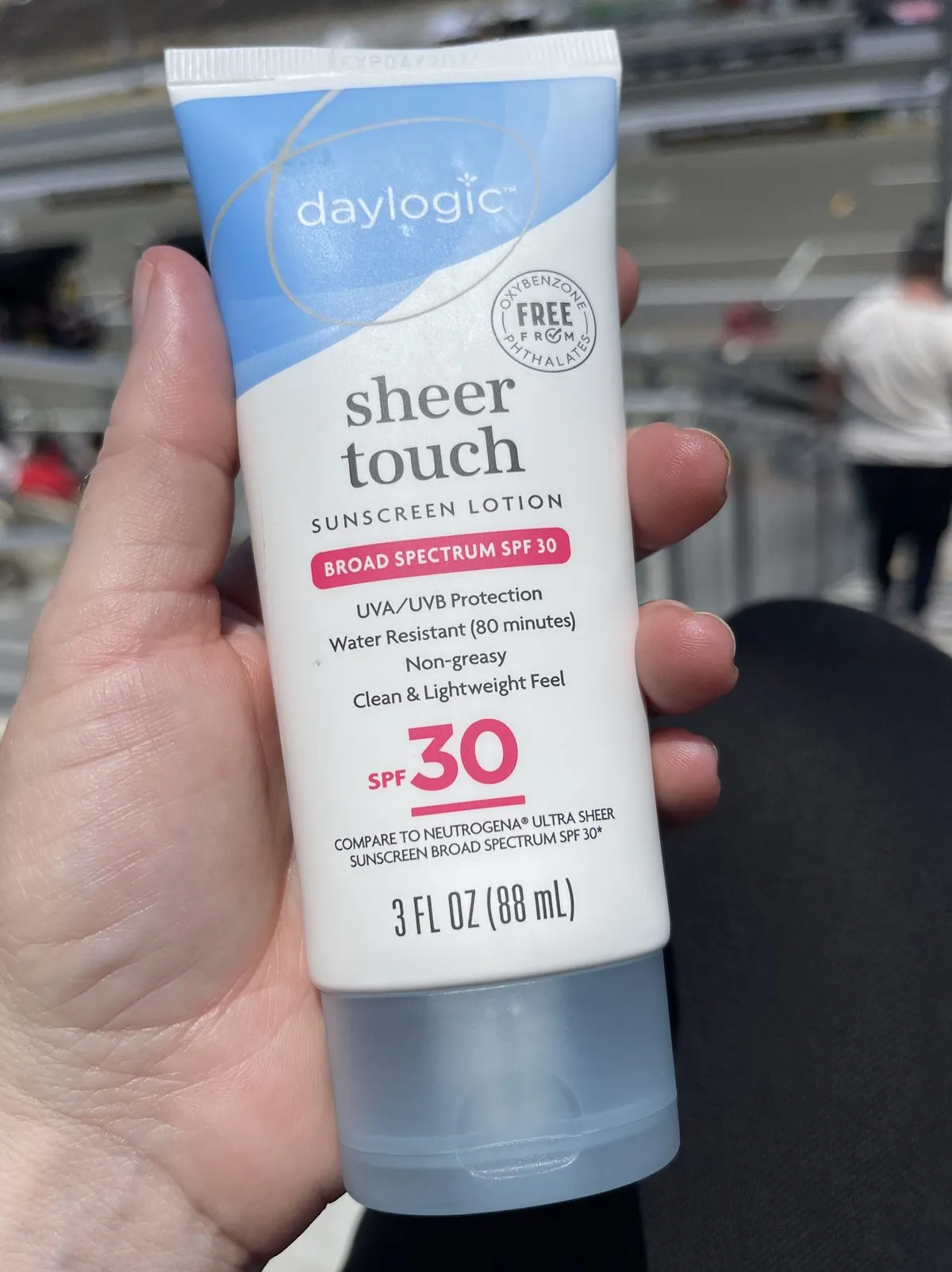 A hand holding a white and blue store-brand sunscreen tube, the front panel reading Broad Spectrum SPF 30, UVA/UVB Protection, and Water Resistant 80 minutes