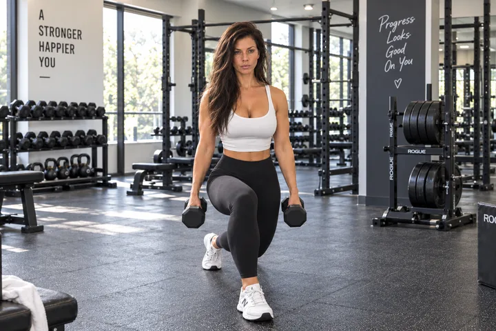 A woman performing a lunge while holding dumbbells in a gym