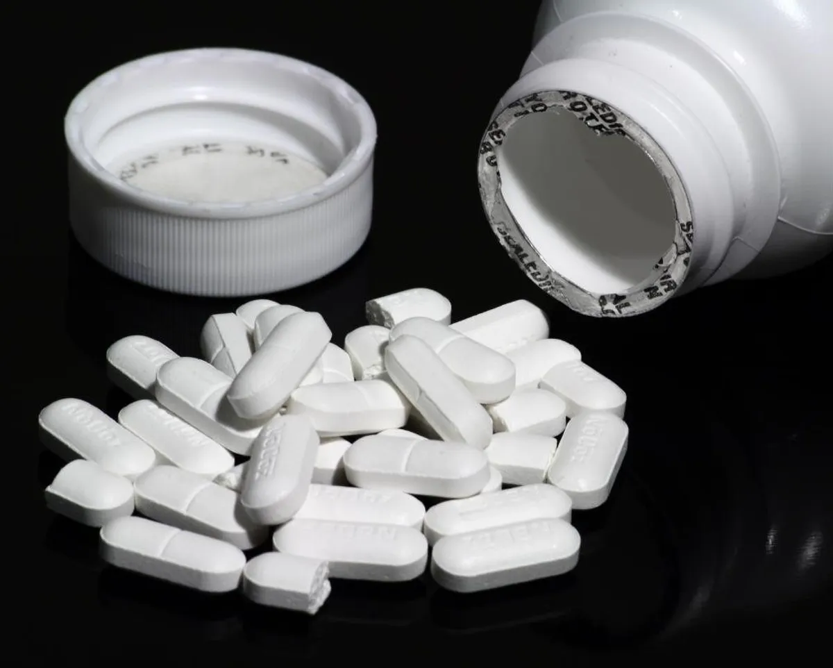 White caffeine tablets spilling from an opened bottle onto a black surface