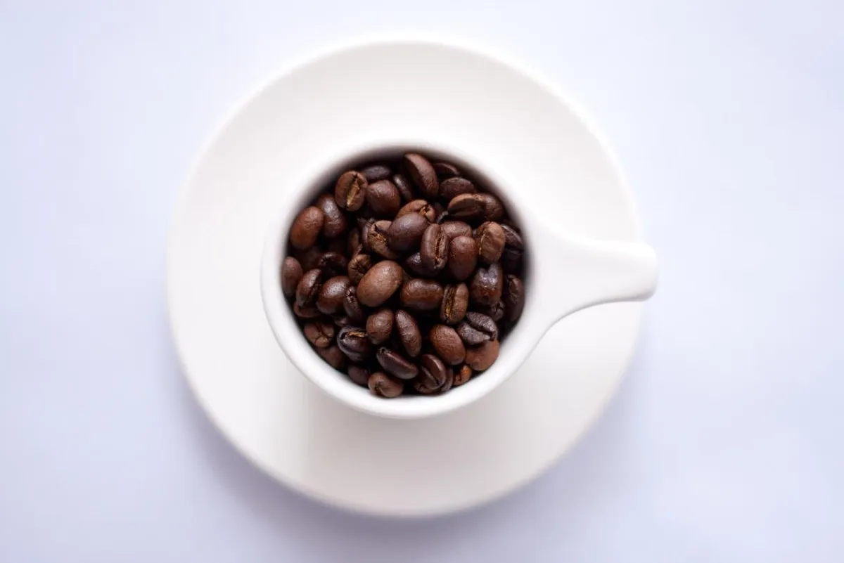 An overhead view of a white cup and saucer filled with roasted coffee beans