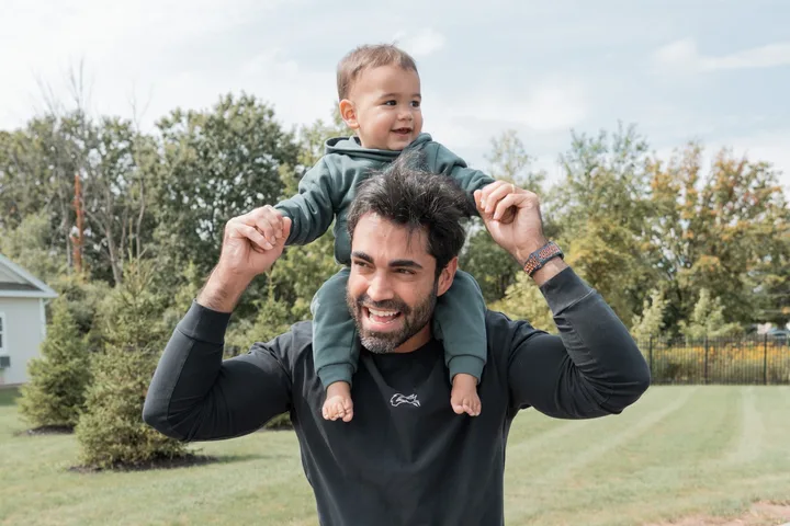 Igor Deoli carrying his child on his shoulders outdoors